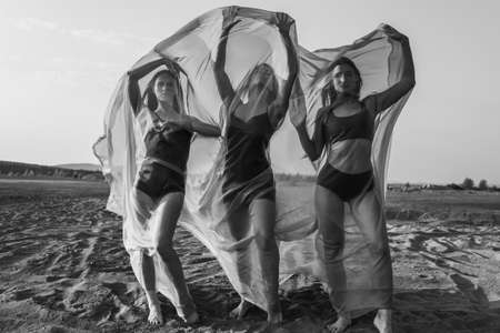 Three girls in flowing fabric pose on sand duneの写真素材