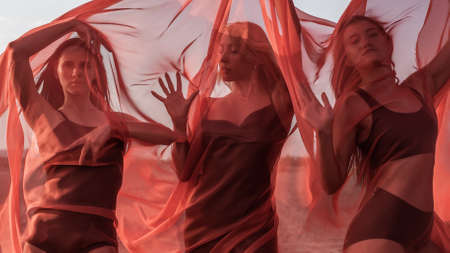 Three girls in red flowing fabric romantic pose and dance on sand duneの写真素材