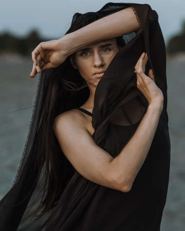 Portrait of the young woman covered flying black fabric on sand dune