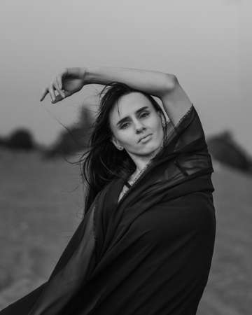 Portrait of the young woman covered flying black fabric on sand dune. black and whiteの写真素材