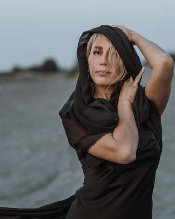 Portrait of the young woman covered flying black fabric on sand duneの写真素材