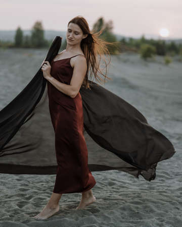 Woman in black with flying fabric dancing on the sand duneの写真素材