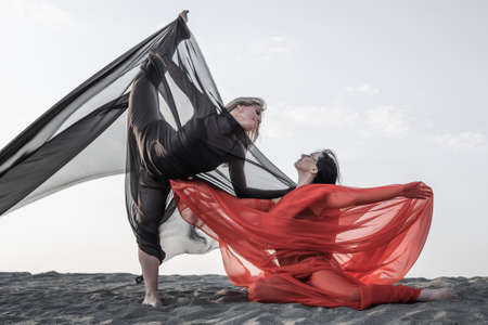 Two girls in black and red flowing fabric romantic pose and dance on sand dune