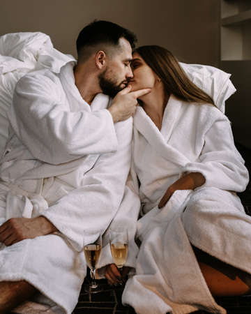 Happy young couple hugging and kissing sitting on floor near the bed in hotelの写真素材