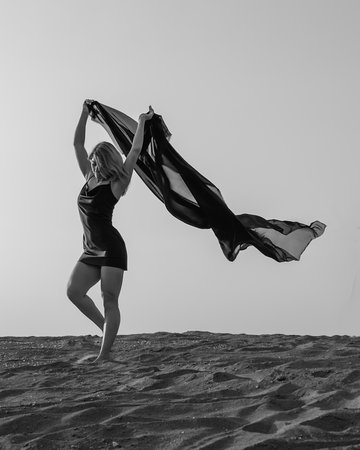 Woman in black with flying fabric dancing on the sand dune. black and whiteの写真素材