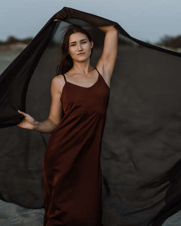 Portrait of the young woman against flying black fabric on sand duneの写真素材