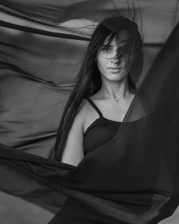 Portrait of the young woman covered flying black fabric on sand dune. black and whiteの写真素材
