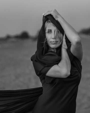 Portrait of the young woman covered flying black fabric on sand dune. black and whiteの写真素材