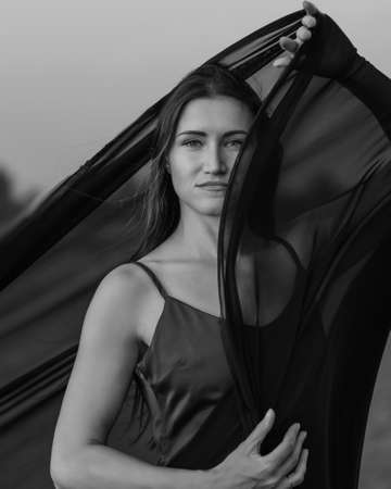 Portrait of the young woman against flying black fabric on sand dune. black and whiteの写真素材