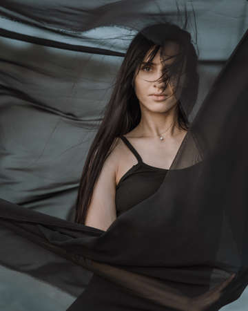 Portrait of the young woman covered flying black fabric on sand duneの写真素材