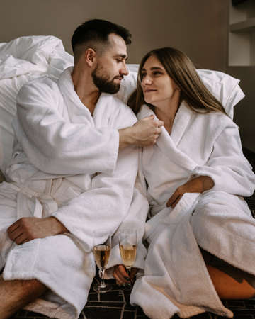 Happy young couple hugging and kissing sitting on the floor near the bed in hotelの写真素材