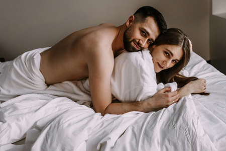European couple hugging together while lying in bed at hotel apartmentの写真素材