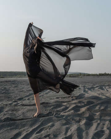 Woman in black with flying fabric dancing on the sand duneの写真素材