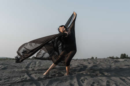 Woman in black with flying fabric dancing on the sand duneの写真素材