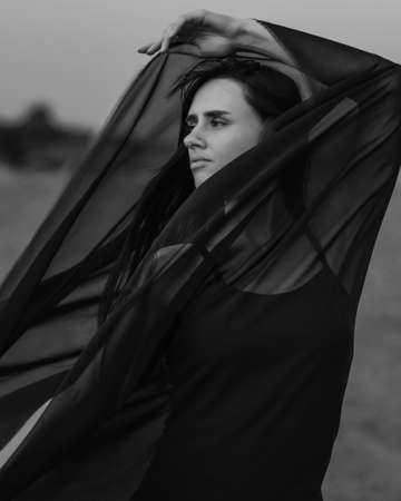 Portrait of the young woman covered flying black fabric on sand duneの写真素材
