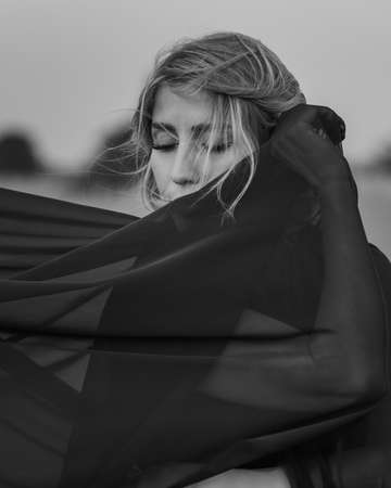 Portrait of the young woman covered flying black fabric on sand dune. black and whiteの写真素材