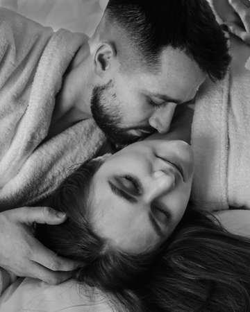 Portrait of young sexy loving couple in bathrobes relaxing on bed at hotel. black and whiteの写真素材