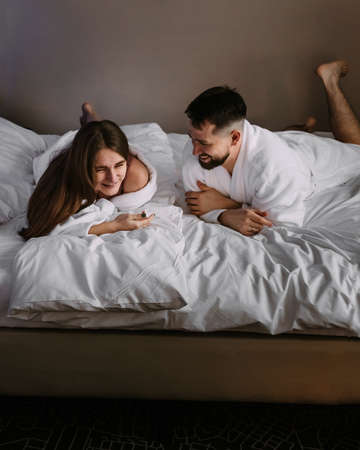 Happy couple having fun and joking looking each other on the bed of hotel roomの写真素材