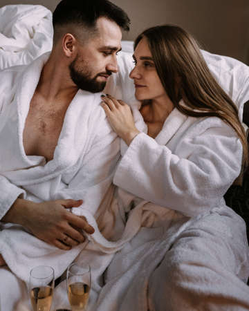 Portrait of happy young couple hugging and kissing sitting on the floor near the bed in hotelの写真素材