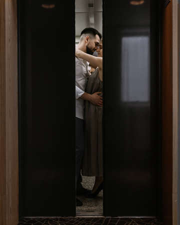 Young stylish caucasian couple hugging and kissing in hotels elevator.の写真素材