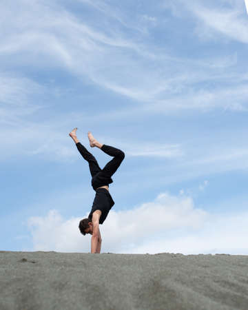 Young man stands on hands on the sand in desert at horizonの写真素材