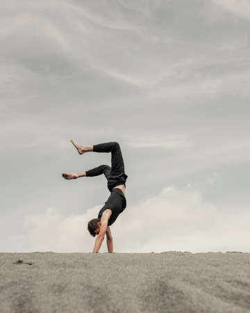 Young man stands on hands on the sand in desert at horizonの写真素材
