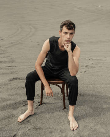 Lone young man sitting on chair in desertの写真素材