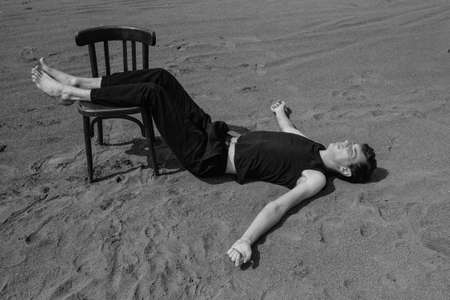 Lone young man lying on chair in desert. black and whiteの写真素材