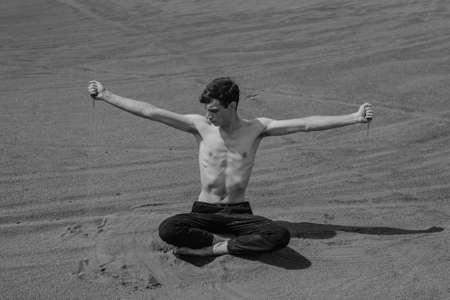Man sitting on the sand dune and pouring sand through hand in desert. black and whiteの写真素材