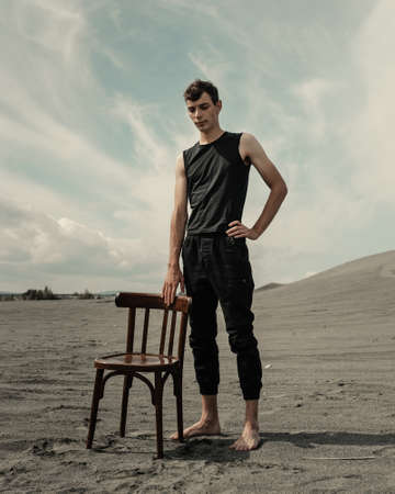 Lone young Man staying near chair in desertの写真素材