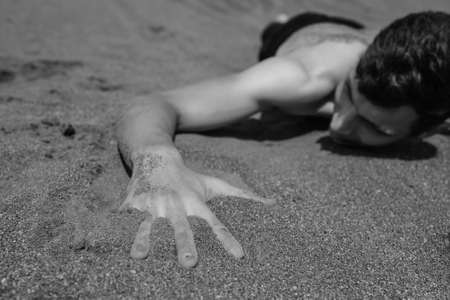 Young Man lying on his stomach on sand in desert.Selective focus on hand in foreground. black and whiteの写真素材