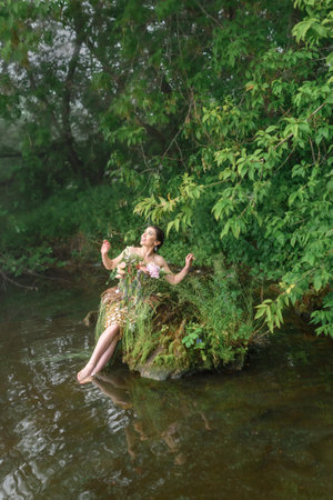 Blooming gorgeous lady in dress of flowers by the lake in the forest in the morning fog. forest fairyの写真素材