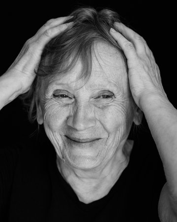 Portrait of senior smiling caucasian woman with hand on head on black background. Close up, black...