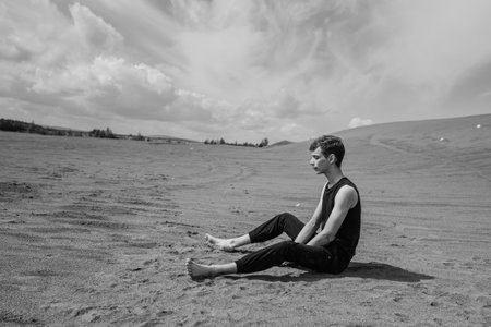 Lone man sitting barefoot on the sand in sandy desert. black and whiteの写真素材