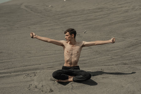 Man sitting on the sand dune and pouring sand through hand in desertの写真素材