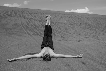 Lone young Man lying on sand with his legs up in desert. black and whiteの写真素材