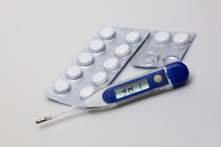 Digital thermometer with pills in a blister pack on a gray background closeupの写真素材