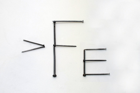 Sign "> Fe" on a white background of iron nailsの写真素材