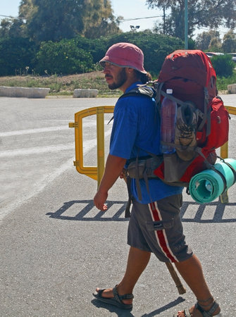 A walking bearded tourist with a big red backpack and a staff in his right hand.のeditorial素材