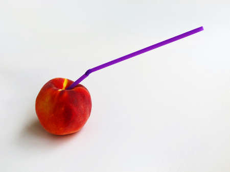 Red-yellow ripe peach with a purple straw stuck into it on a gray backgroundの写真素材