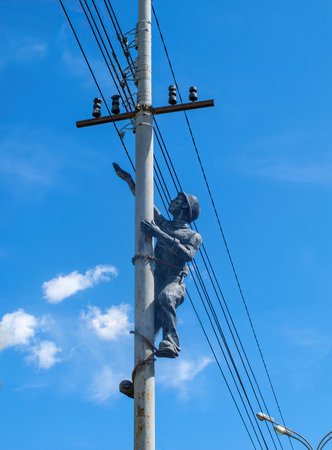 Sculpture in gray cast iron of an electrician on a street pole with electric wires.のeditorial素材