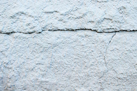 Cement wall painted with white paint with cracks. Natural background. Abstract vintage backdrop.の写真素材