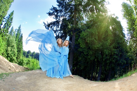 Two woman, twins in the forest in a blue flowing dressの写真素材