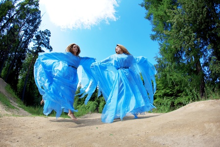 Two woman, twins in the forest in a blue flowing dressの写真素材