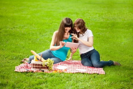 Two women in the park on a picnic and Tablet PCの写真素材