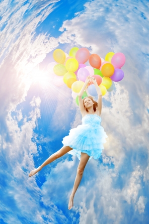 Woman holding balloons against sun and skyの写真素材
