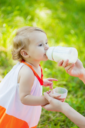 Mother feeds baby girl outdoors in the grassの写真素材