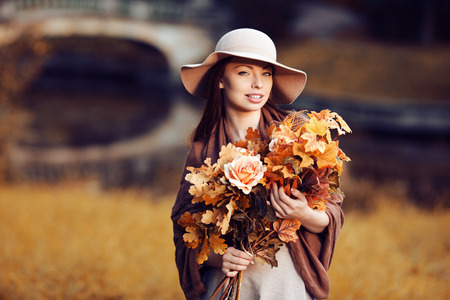 Young fashion woman  walking in autumn park with a bouquet of fall leaves of maple and oak autumn roses.の写真素材