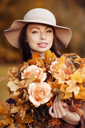 Young fashion woman  walking in autumn park with a bouquet of fall leaves of maple and oak autumn roses.の写真素材