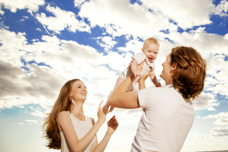 Happy family throws up baby boy against blue sky and white clouds